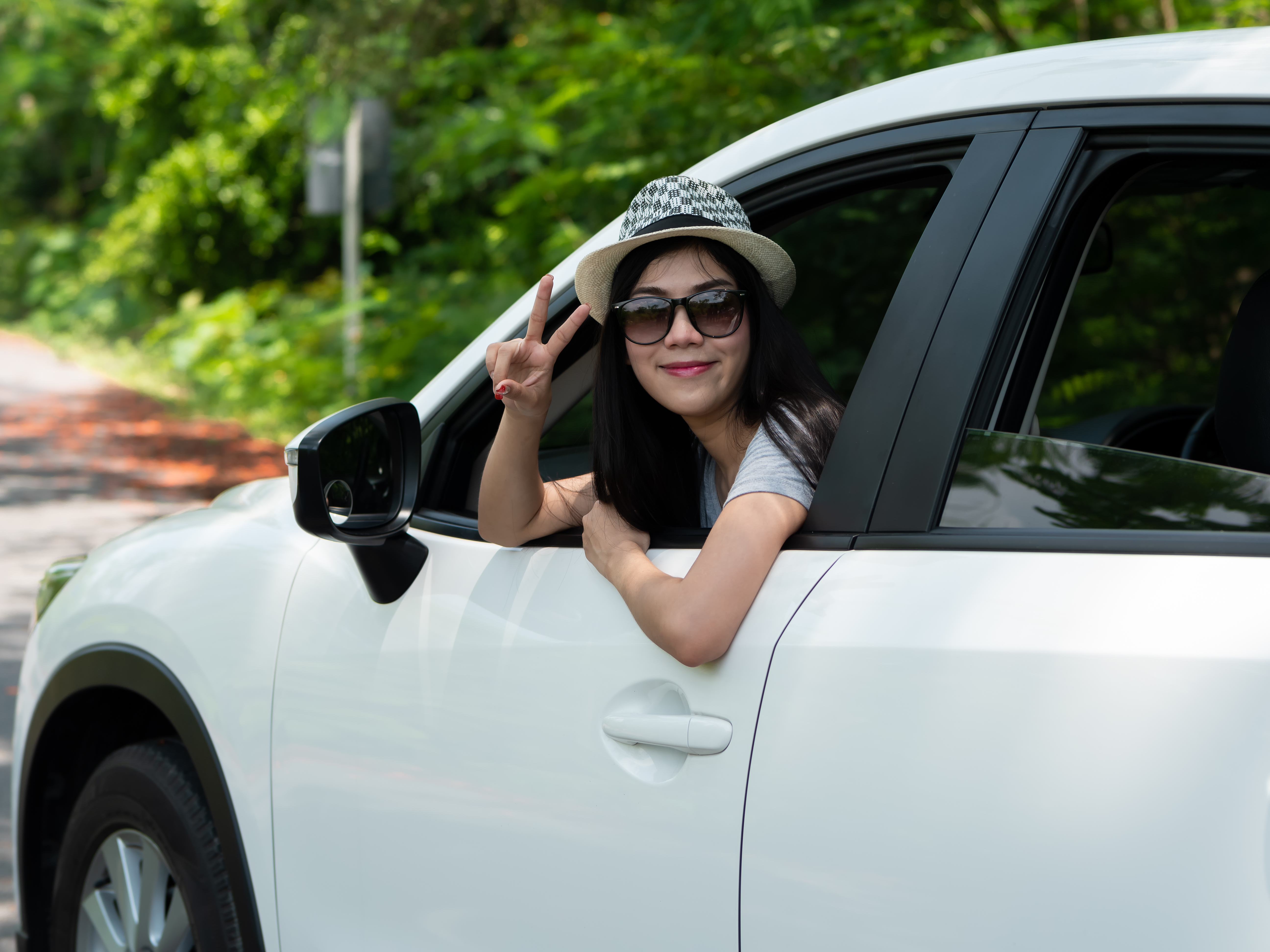happy woman showing peace sign with her head out of the window of a car