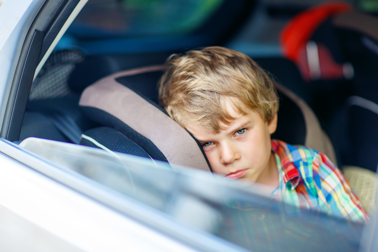 Sad tired kid boy sitting in car during traffic jam